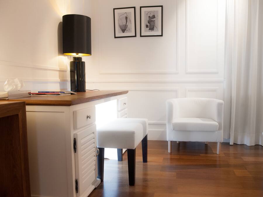A modern bedroom with a wooden desk, a white chair, a bedside table, and a bed.