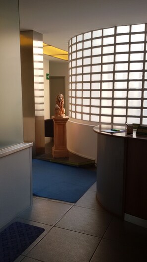 A hotel reception area with a statue, a blue carpet, and a window with a grid pattern. - Hotel Antonelli (Milan)