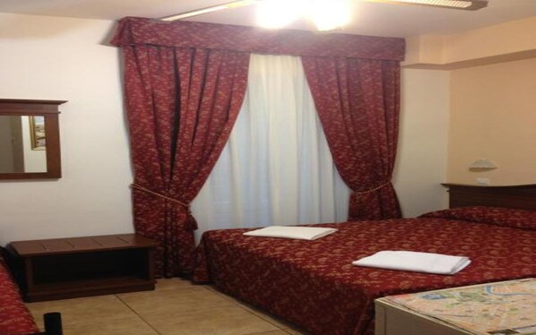 Habitación de hotel con dos camas, una mesita de noche, un espejo y una ventana con cortinas rojas.