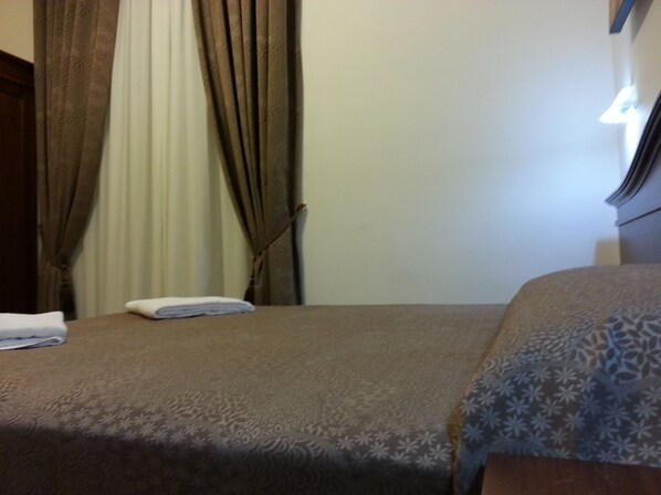 A hotel room with a bed, curtains, and a nightstand.