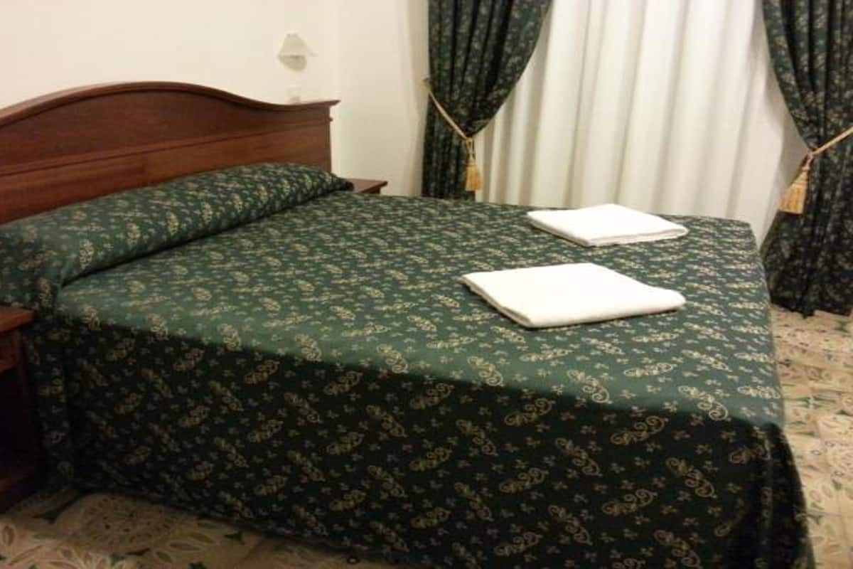 A neatly made bed with a green patterned bedspread and two folded white towels.