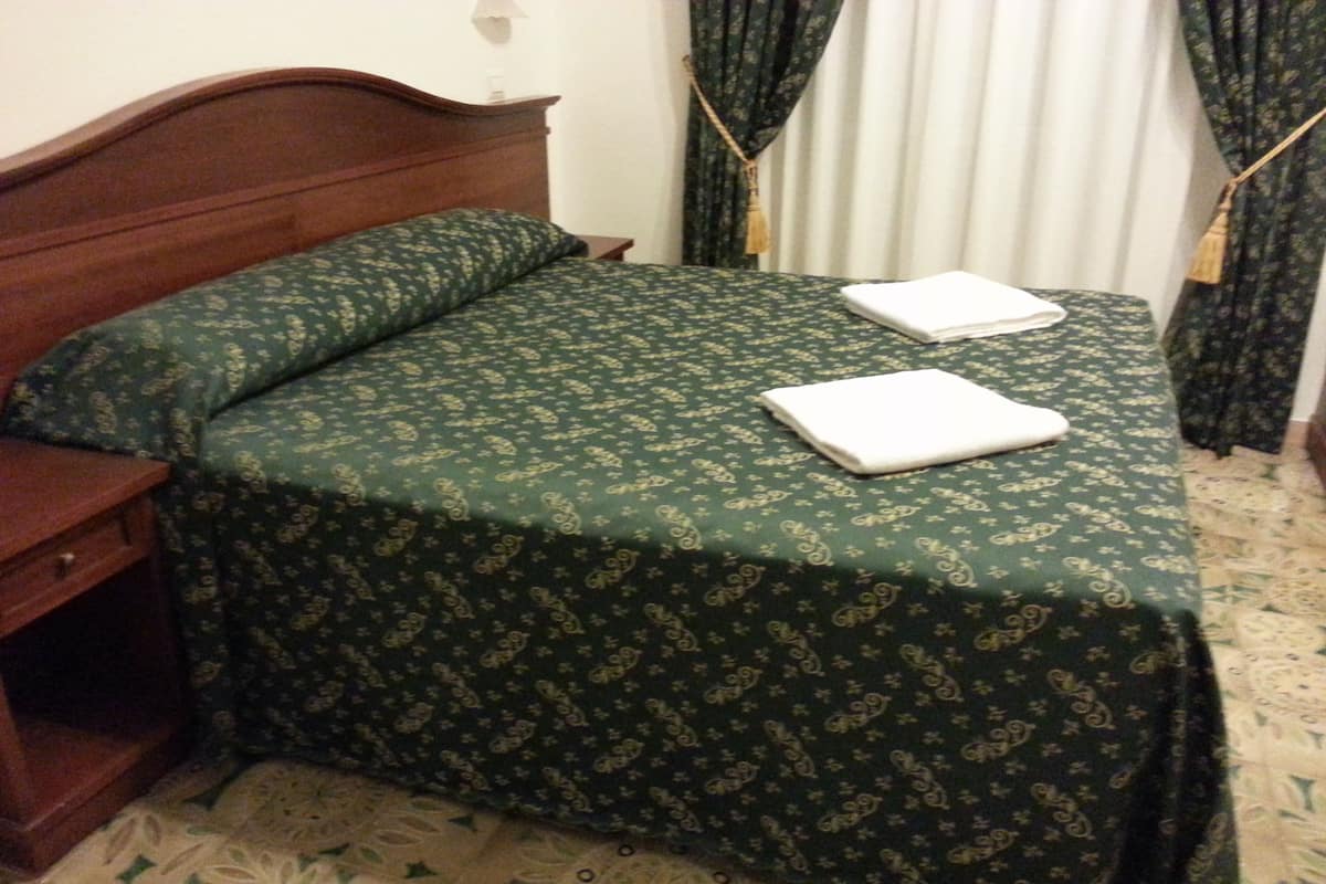 A neatly made bed with a green patterned bedspread and two white towels.