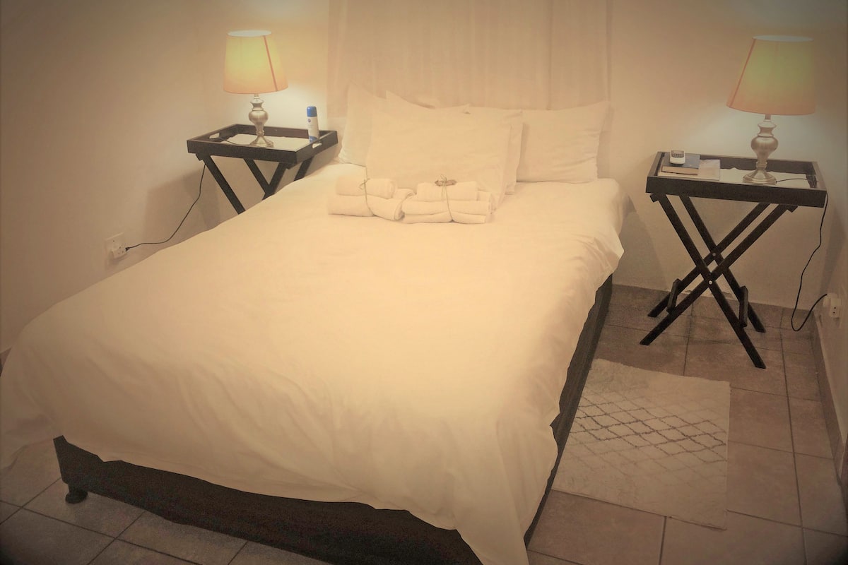Una cama bien hecha con sábanas blancas, dos mesitas de noche con lámparas y una pequeña alfombra en el suelo.