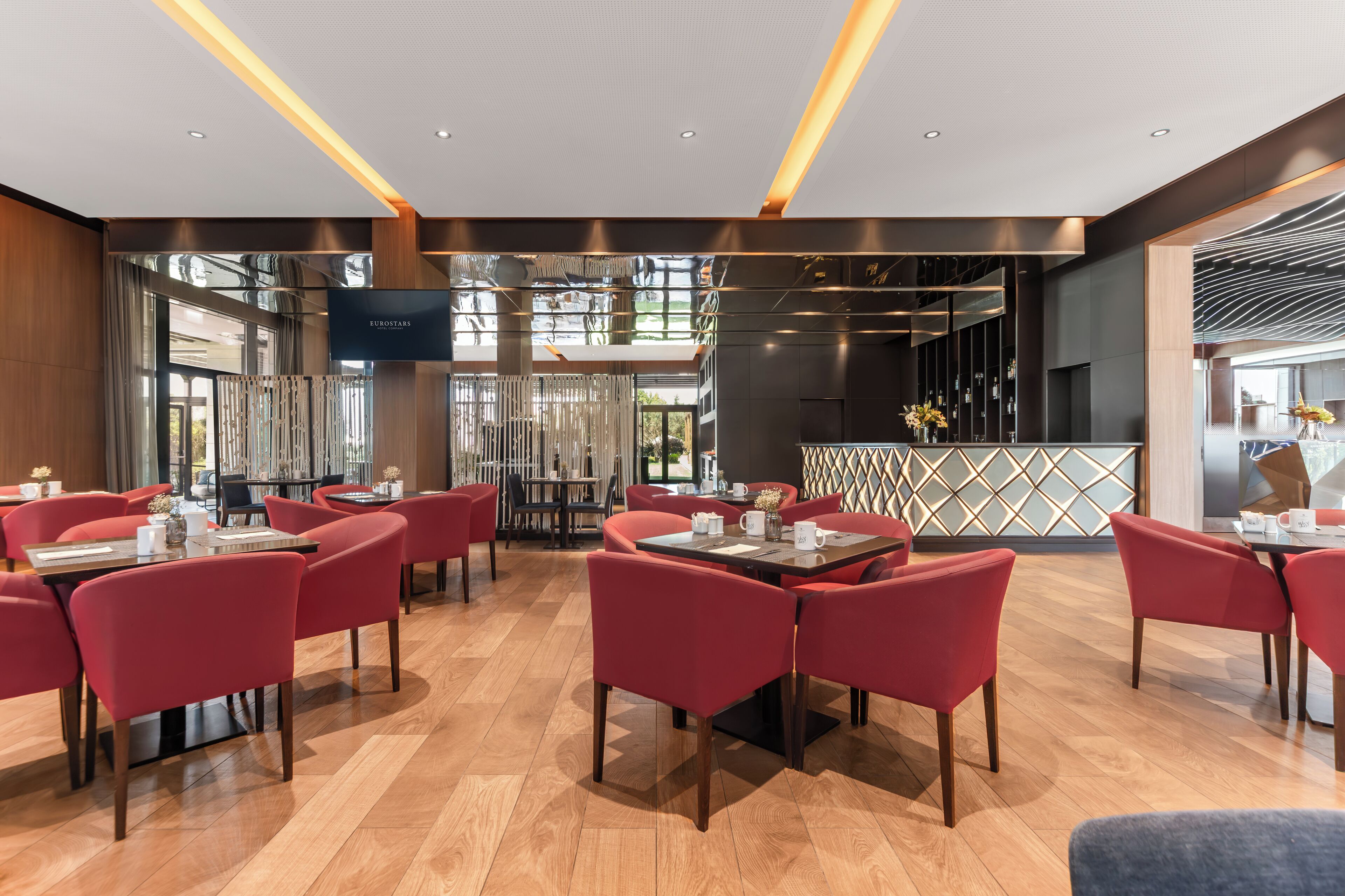 Un restaurante moderno con sillas rojas y mesas de madera, una pantalla de televisión y una pared decorativa.