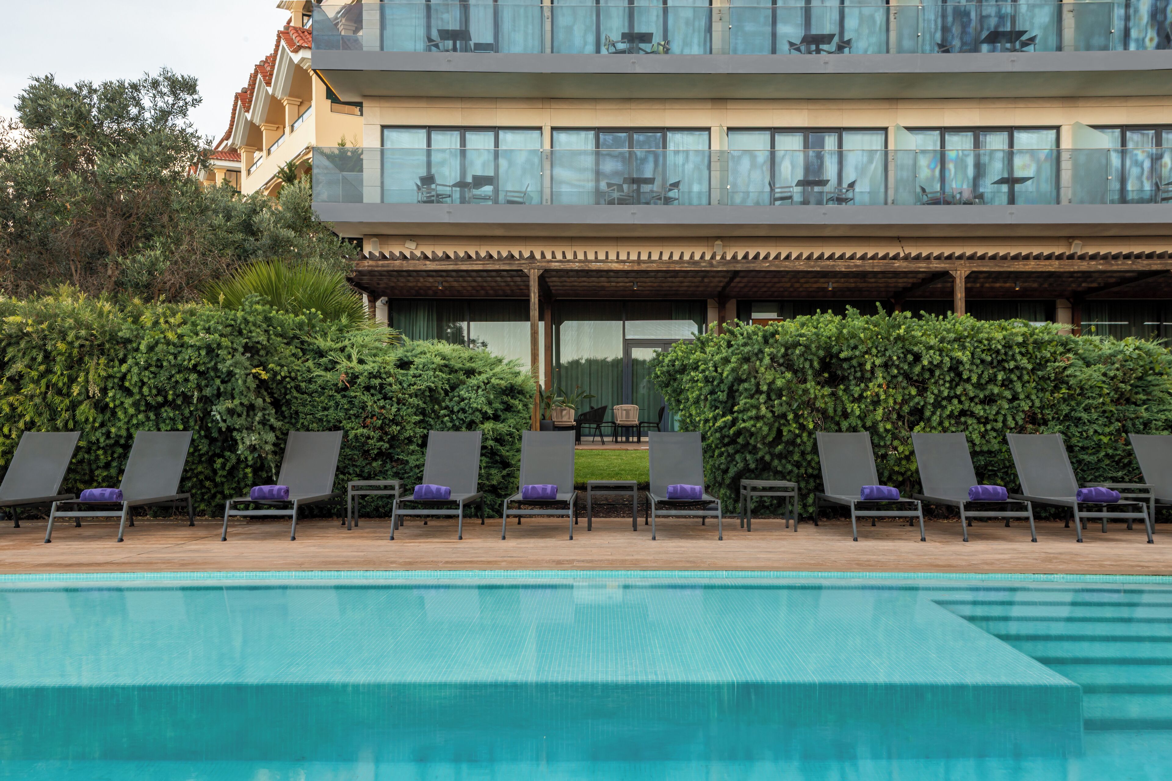 Un hotel moderno con piscina, sillones de descanso y un área exterior techada.