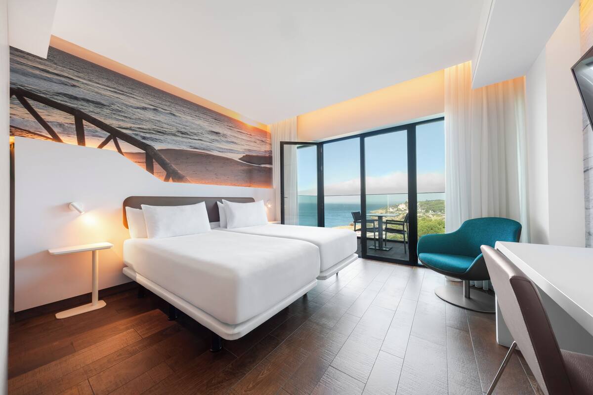 A modern hotel room with a large bed, a desk, and a view of the ocean.