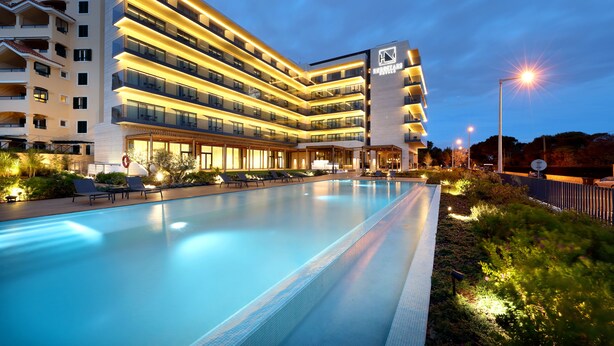 Un hotel moderno con piscina, varios balcones y zonas exteriores bien iluminadas.