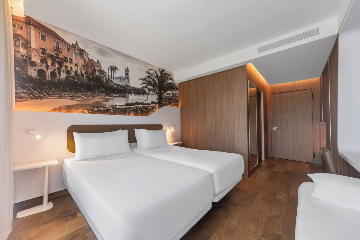 A modern hotel room with a large bed, a nightstand, a wall-mounted painting, and a wooden wardrobe.