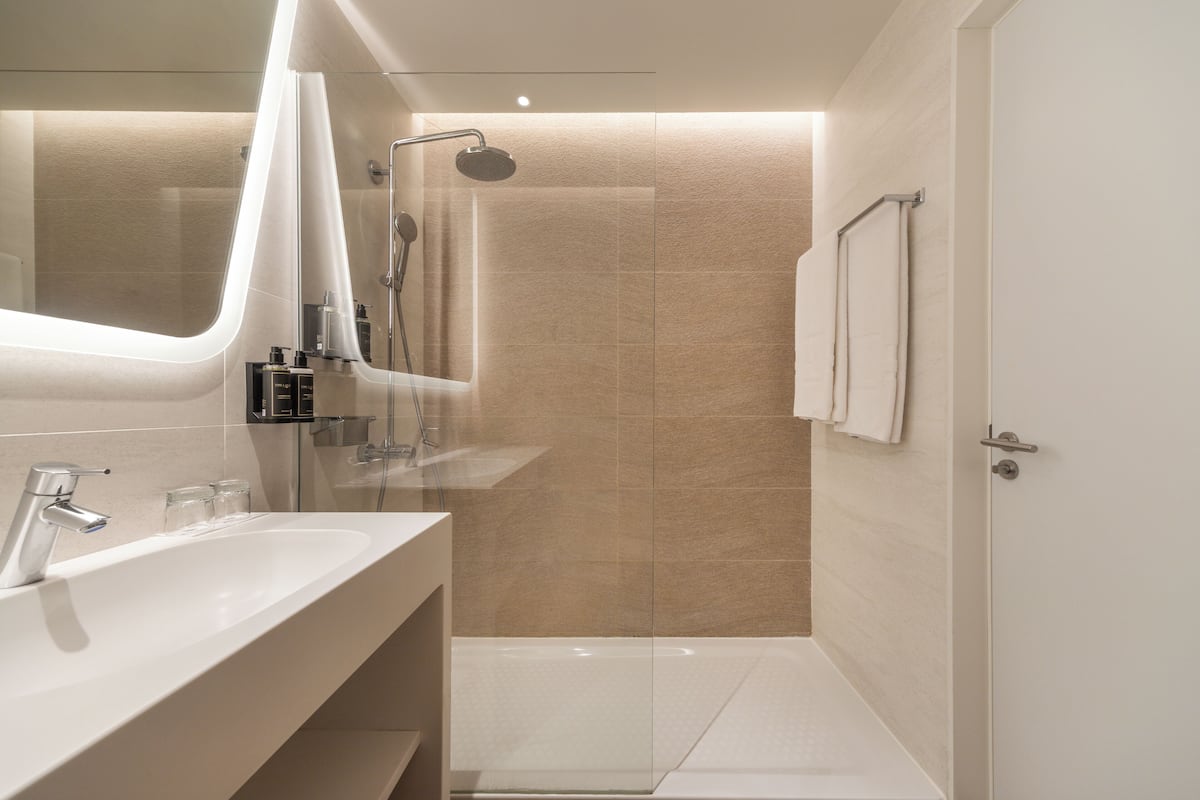 A modern bathroom with a large mirror, two sinks, a shower, and a towel rack.