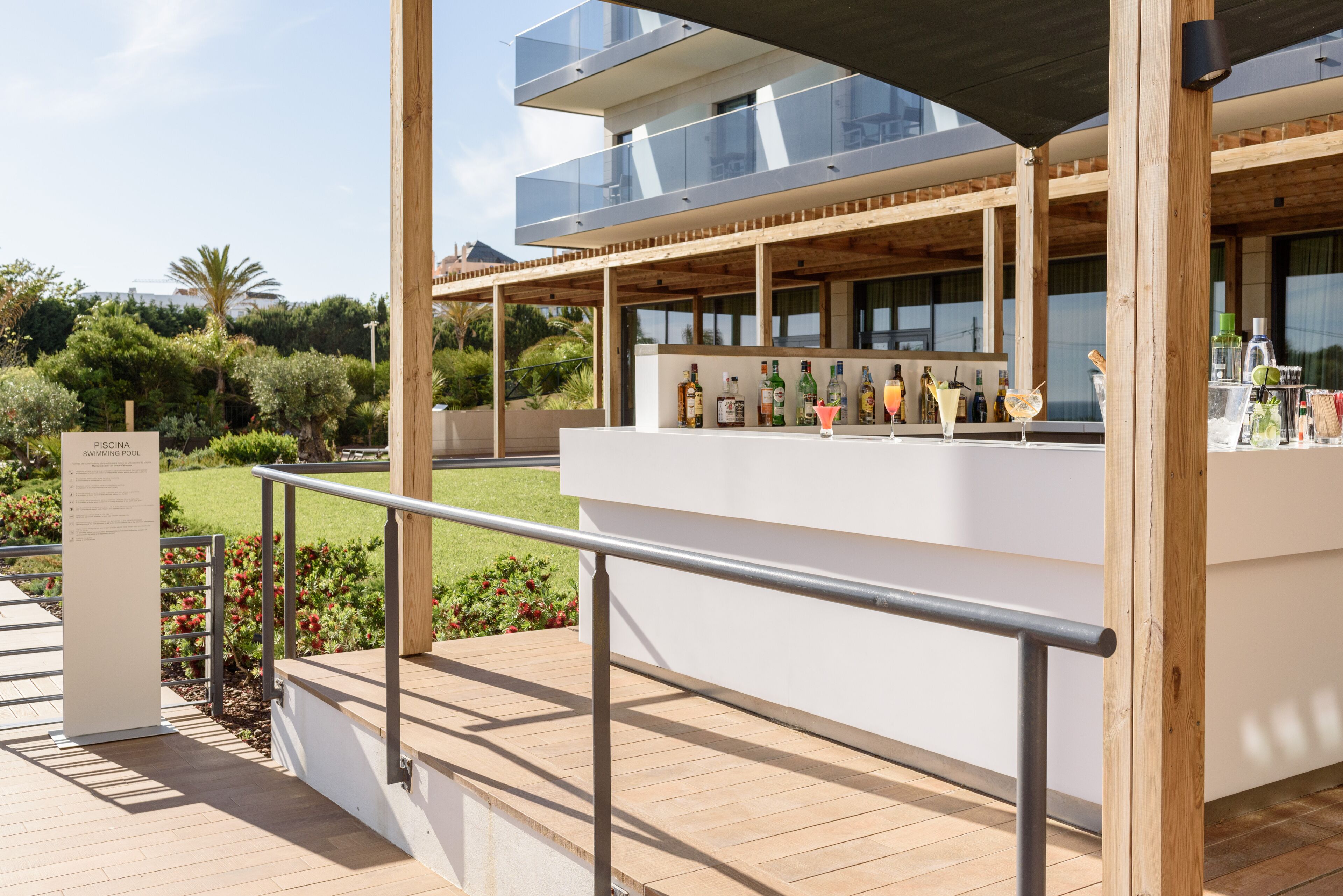 Zona de bar amb un senyal de piscina, terrassa de fusta i mobiliari exterior.