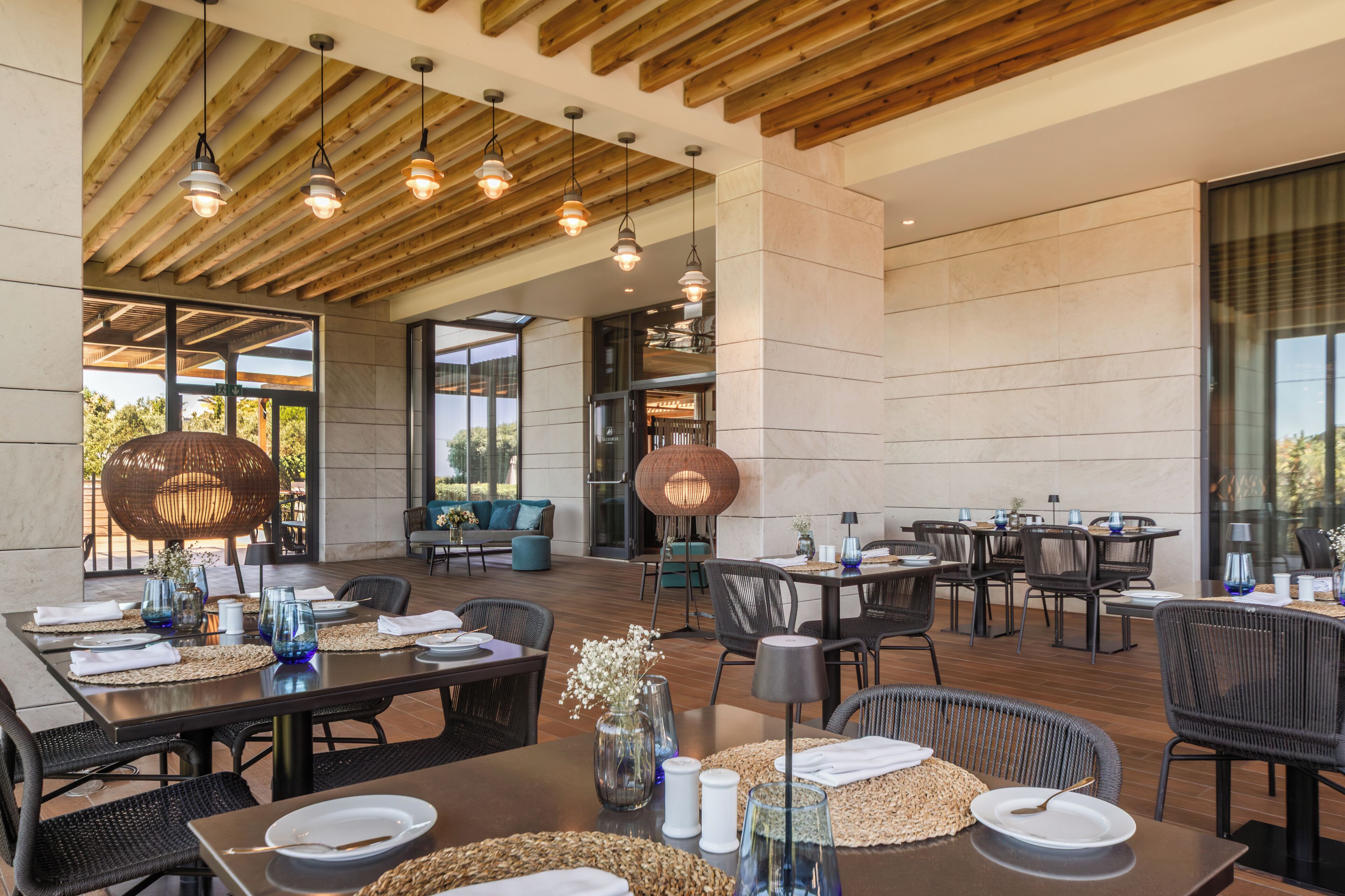 Un espace de restauration en plein air doté de nombreuses tables et chaises, de poutres en bois au plafond et de grandes fenêtres.