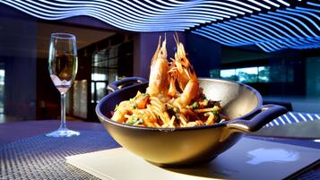 Un plato de pasta con camarones sobre una mesa con una copa de vino y una computadora portátil.