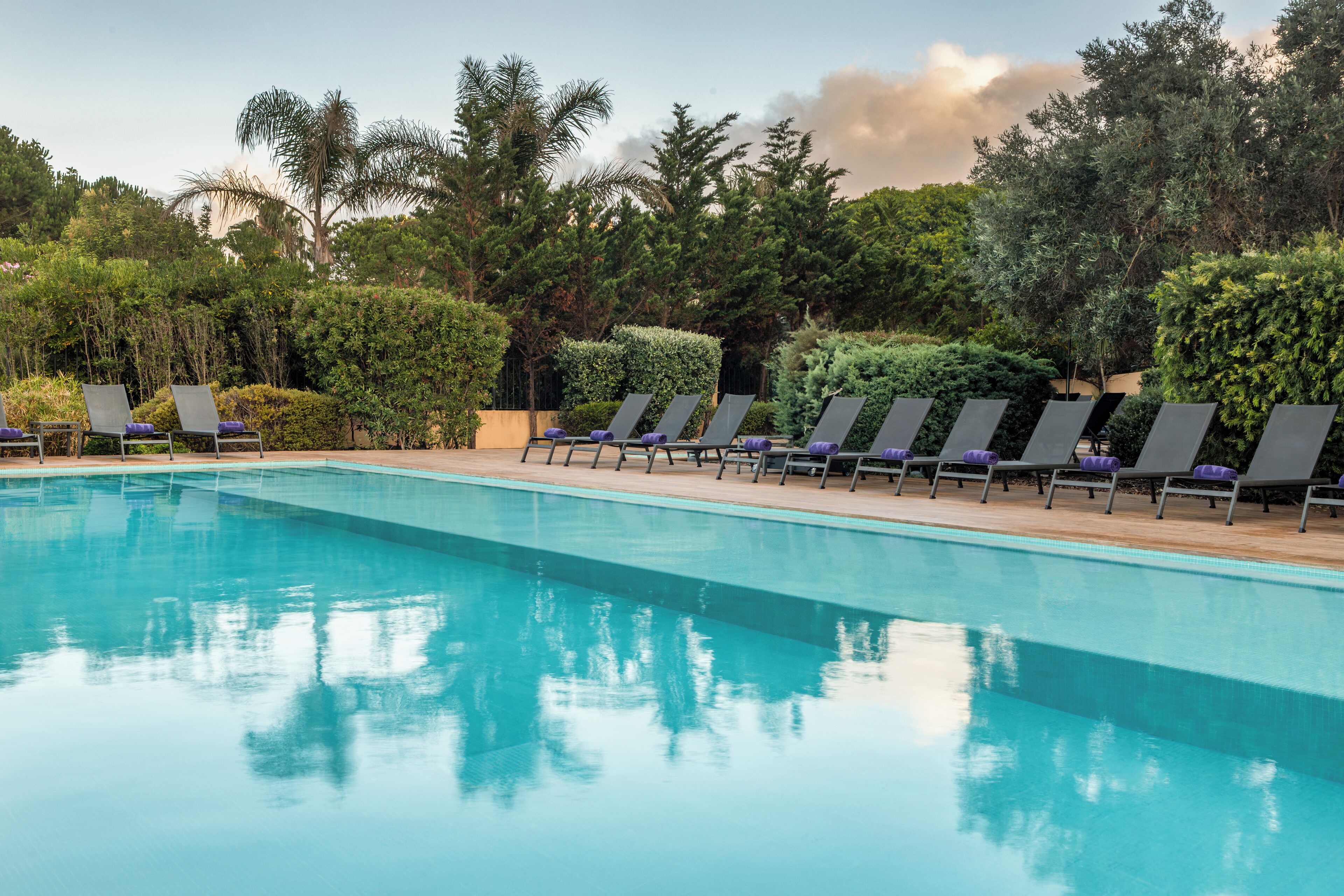 A swimming pool with lounge chairs and greenery.