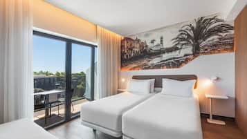 A hotel room with a balcony, two beds, a painting of a coastal scene, and a nightstand with a lamp.