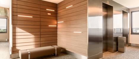 A modern office space with a wooden panel wall, a bench, and an elevator.