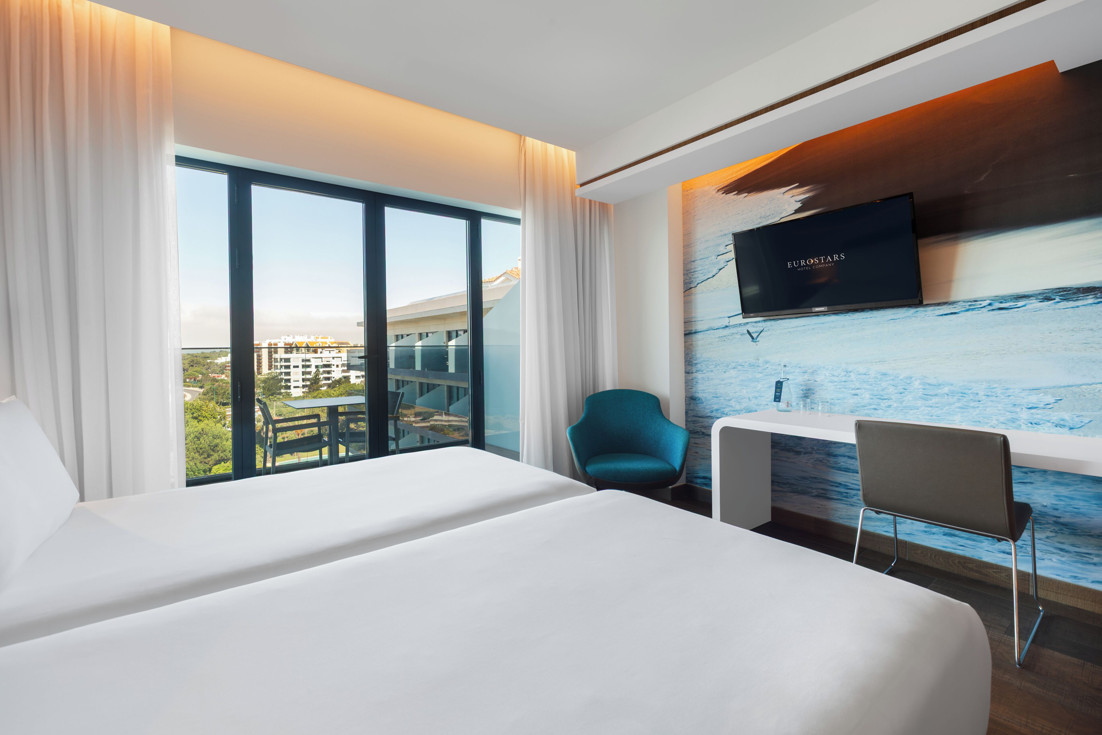 A hotel room with a large bed, a desk, a chair, and a TV mounted on the wall.