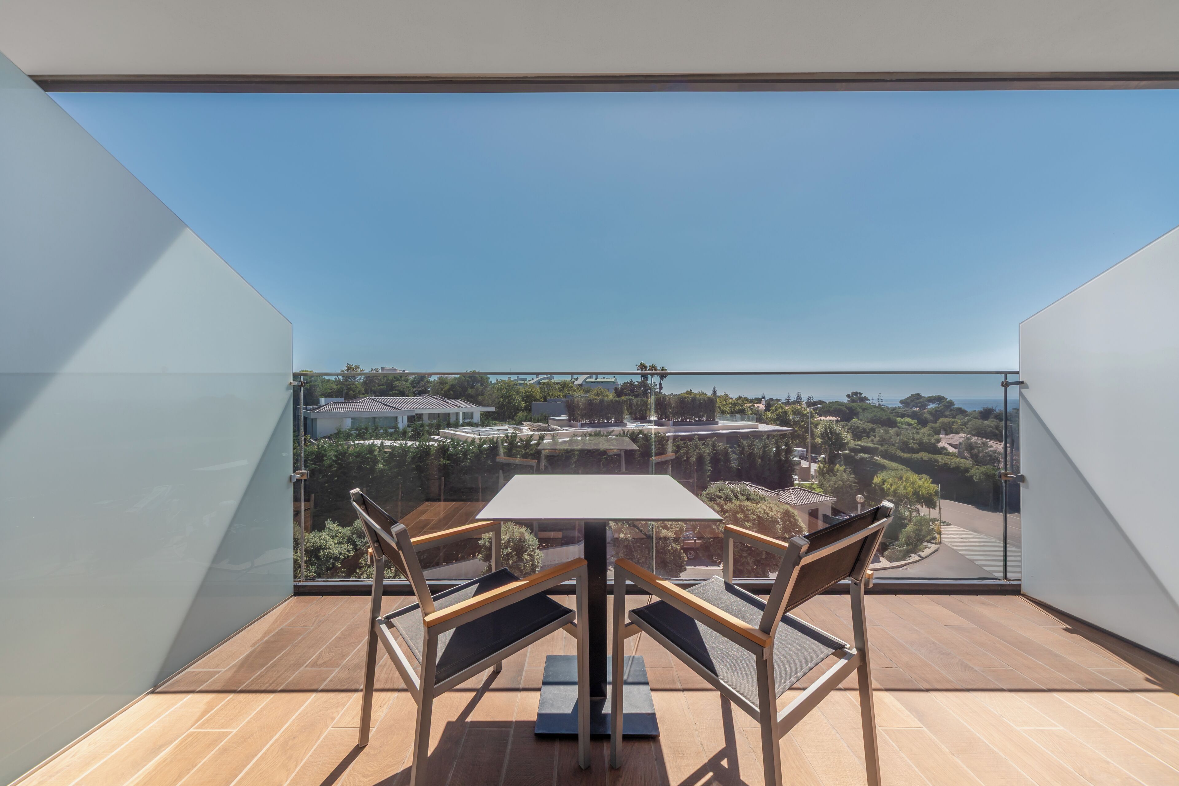 Un balcón con mesa y sillas, con vistas a una zona residencial con casas y vegetación.
