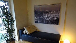 A modern living room with a dark sofa, a potted plant, and a cityscape painting on the wall. - Hannover Guest House (Hannover)