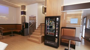 Een hotellobby met een automaat, zithoeken en een trap.