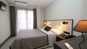 Een hotelkamer met een bed, een bureau, een lamp, een telefoon en een airconditioner.