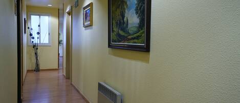 A hallway with wooden flooring, a radiator, and two framed pictures on the walls.