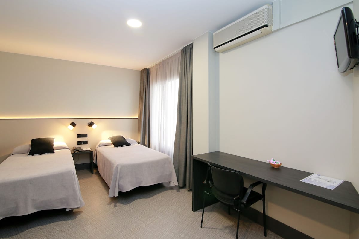 Habitación de hotel con dos camas individuales, un escritorio, una silla, un teléfono y un equipo de aire acondicionado.