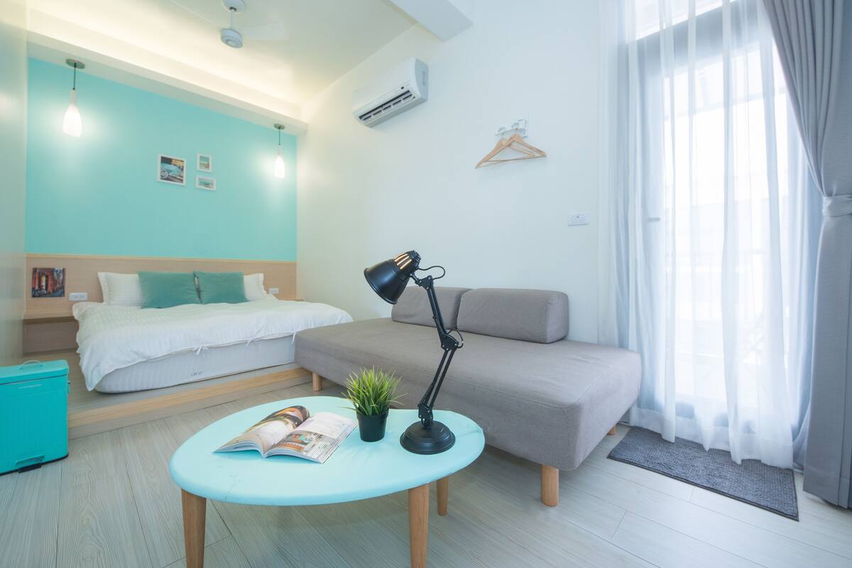 A modern bedroom with a bed, a sofa, a desk with a lamp, and a small plant.