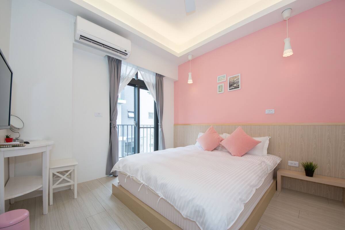 A bedroom with a bed, a desk, a small stool, a bench, and a potted plant.