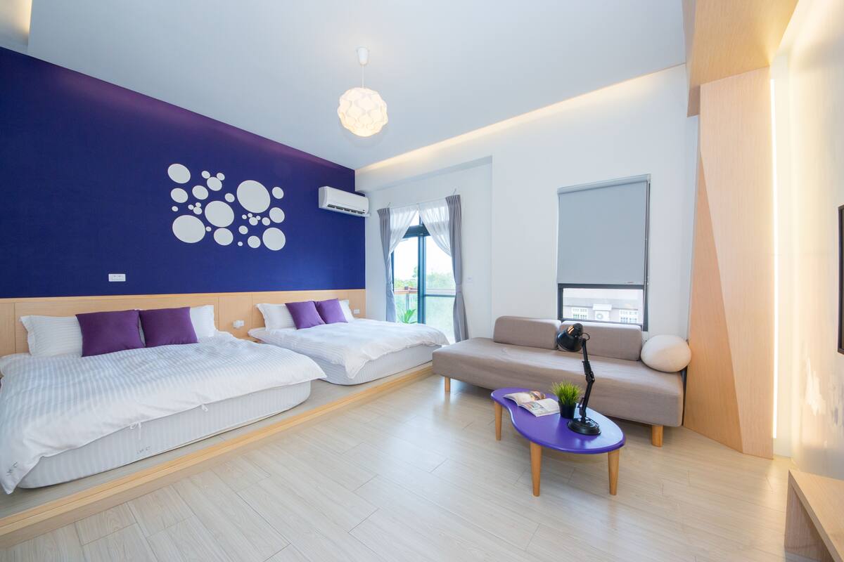 A modern hotel room with a bed, sofa, and a small table with a lamp.