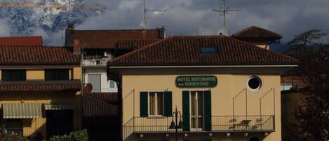 A hotel named "HOTEL RISTORANTE FIORENTINO" with a balcony, a mountain in the background, and a construction crane nearby.