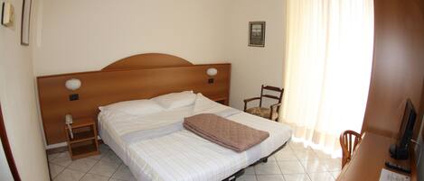 A bedroom with a bed, a chair, a desk, a telephone, and a window with curtains.