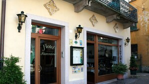 A hotel facade with a wooden door labeled "Hotel Fiorentino," a restaurant sign, and a balcony with decorative ironwork.