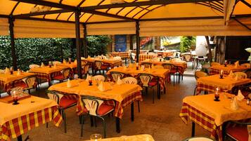 An outdoor dining area with multiple tables covered with yellow tablecloths and red and yellow checkered table runners.