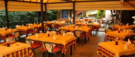 An outdoor dining area with multiple tables covered with yellow tablecloths and red and yellow checkered table runners.