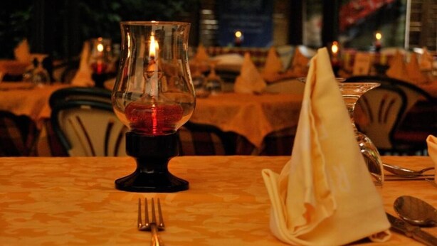 A dining table with a candle in a glass holder, a folded napkin, and cutlery.
