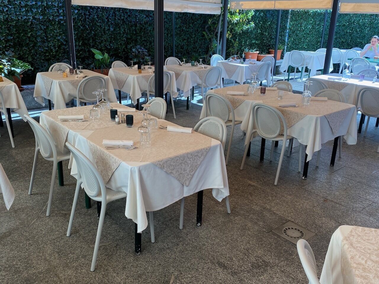 An outdoor dining area with tables and chairs, covered by a canopy.