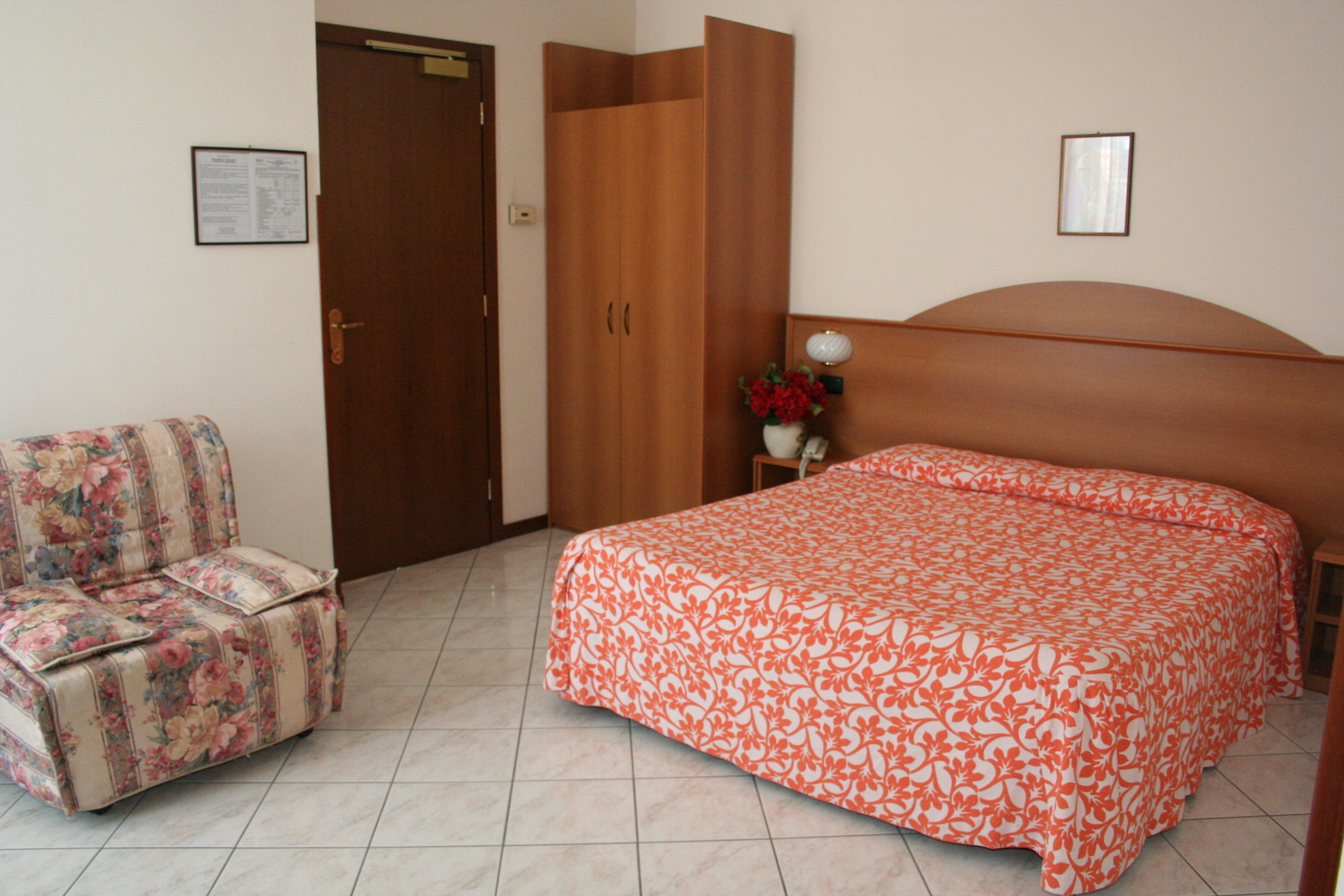Un dormitorio con cama, una silla, un armario y una mesita de noche con un jarrón.