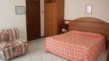 Un dormitorio con cama, una silla, un armario y una mesita de noche con un jarrón.