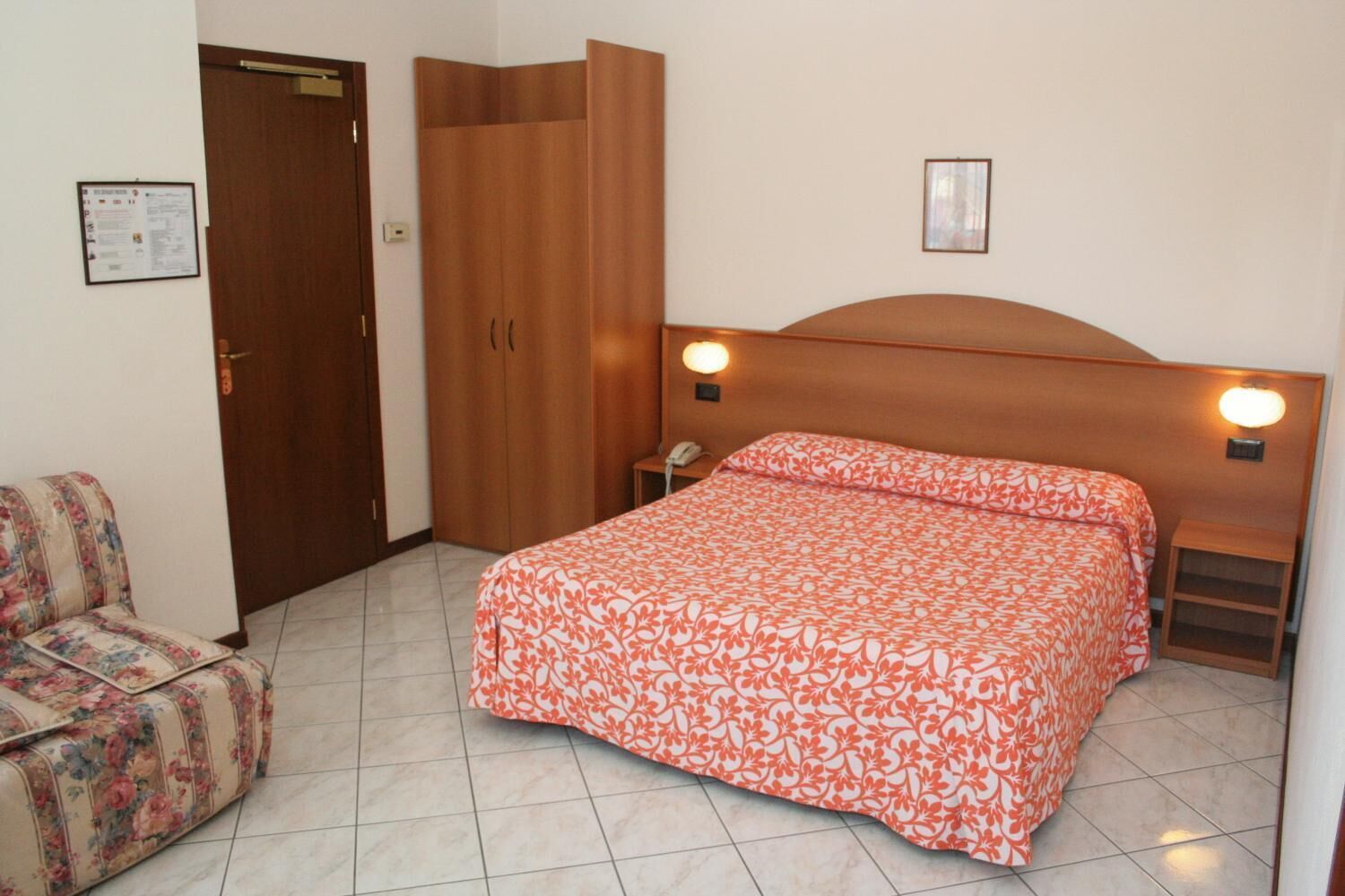A bedroom with a bed, a chair, a wardrobe, and a nightstand with a lamp.