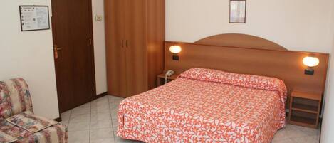 Une chambre à coucher comprenant un lit, une chaise, une armoire et une table de chevet avec une lampe.