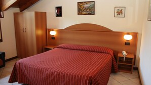 A bedroom with a large bed, wooden headboard, two bedside tables with lamps, a wardrobe, and artwork on the walls.