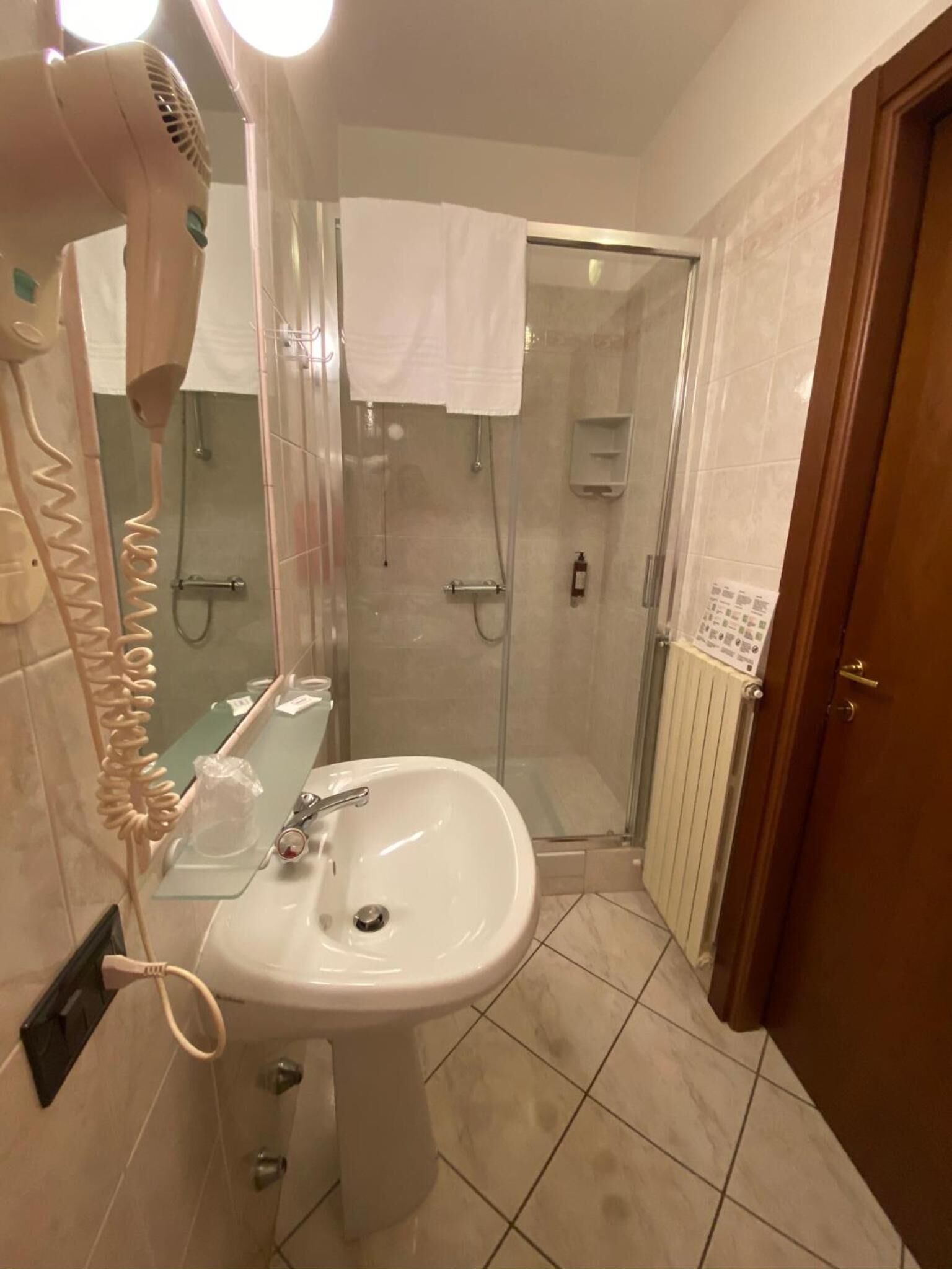 A bathroom with a glass-enclosed shower, a white sink, and a hairdryer on a wall-mounted stand.