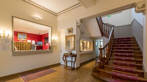 A grand staircase with a red carpet, a wooden floor, and a mirror reflecting a red room with a bookshelf and artwork. - Hôtel Regina (Bordeaux)