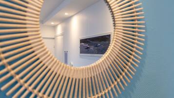 A circular mirror with a wooden frame reflecting a room with a mounted TV and a door.
