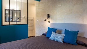 A bedroom with a large bed, two pillows, a wall-mounted light fixture, and a mirror with a window. - Hôtel Regina (Bordeaux)
