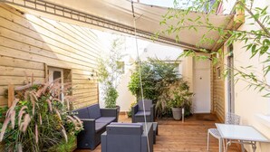 A wooden deck with outdoor furniture, including a sofa and chairs, surrounded by potted plants and a pergola. - Hôtel Regina (Bordeaux)