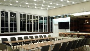 A conference room with a long table and chairs, large windows, a flat-screen TV, and a bar area. - Capital Tirana Hotel (Tirana)