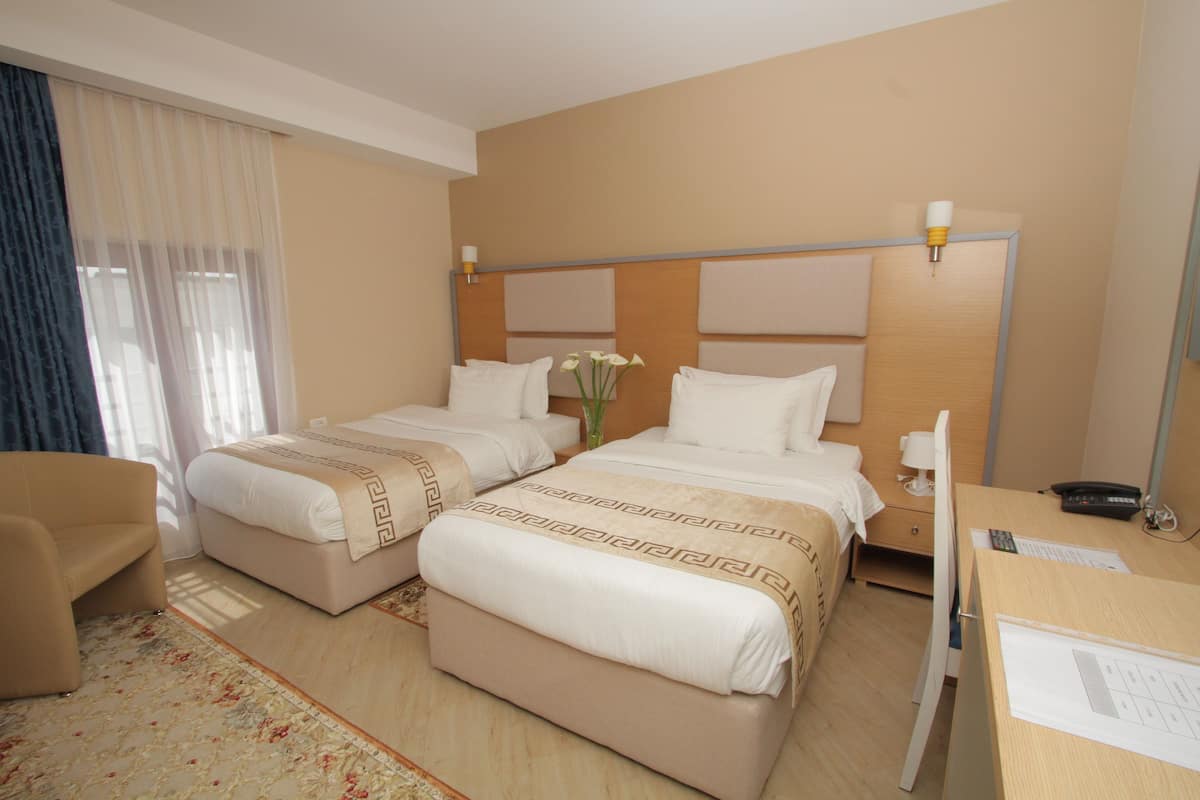 A hotel room with two beds, a desk, a chair, and a window with curtains.