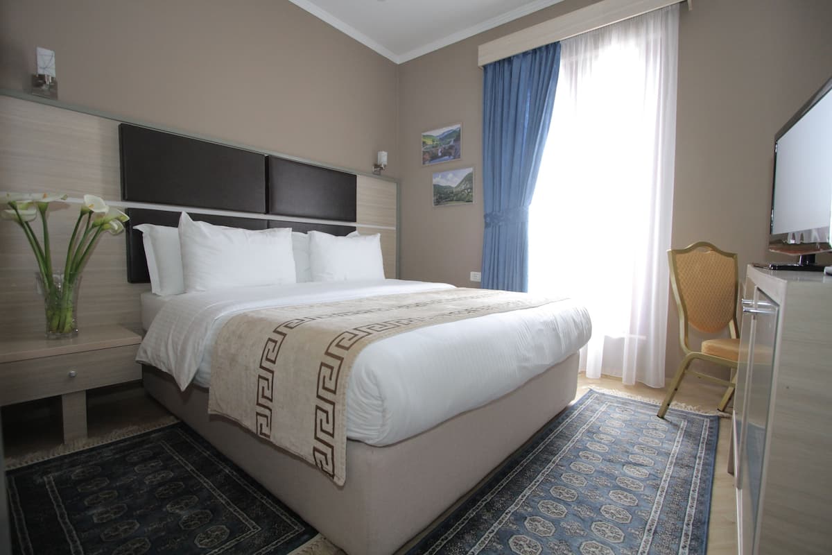 A hotel room with a bed, a desk, a chair, and a TV.
