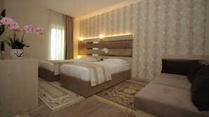 A hotel room with two beds, a sofa, a decorative vase with flowers, and a patterned wallpaper. - Capital Tirana Hotel (Tirana)
